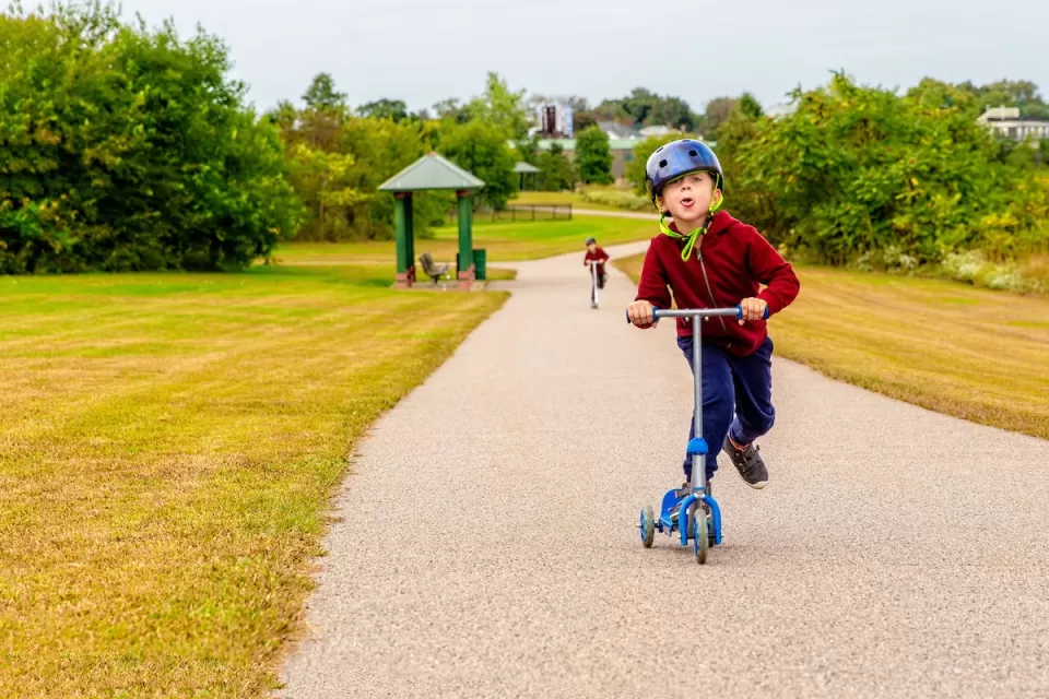 Young child riding scooter on gravel path in park.